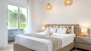 Un dormitorio con cama, mesitas de noche, una ventana con cortinas y dos lámparas colgantes.