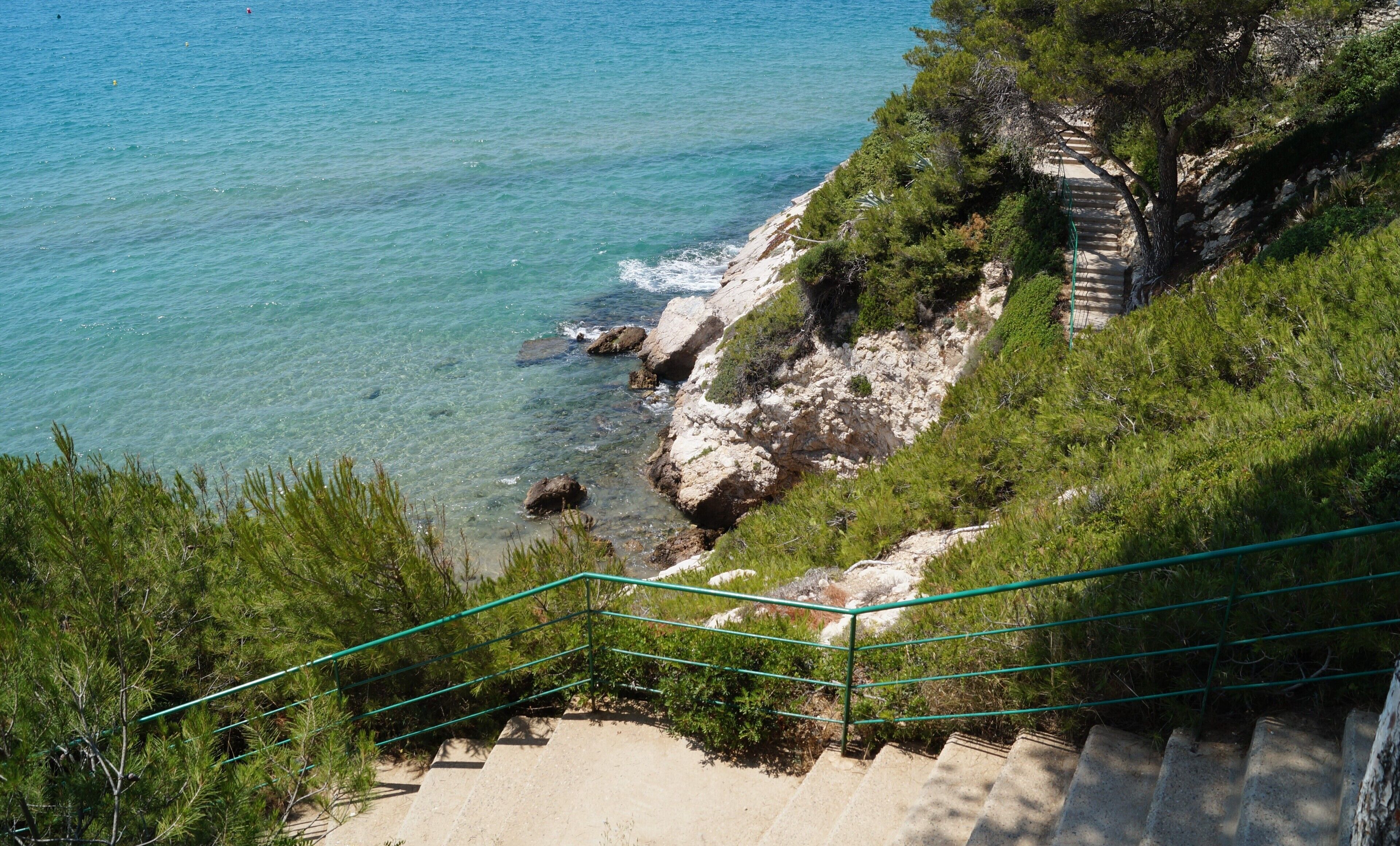 Una scala a picco sul mare che conduce a una spiaggia con acque cristalline e vegetazione.