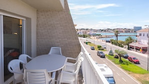 En balkon med et bord og stole, med udsigt over en gade med biler og bygninger nær vandet.