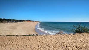 Ein weiter Sandstrand mit sanften Wellen, blauem Himmel und einigen Spaziergängern.