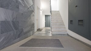 Un couloir moderne avec un mur en marbre, une grille de ventilation en métal et un escalier menant à un ascenseur.