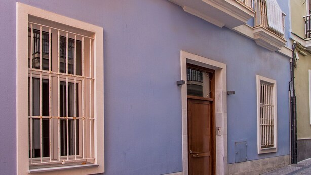 Un bâtiment à deux étages doté d’un balcon, d’une porte en bois et d’une fenêtre avec des barreaux.