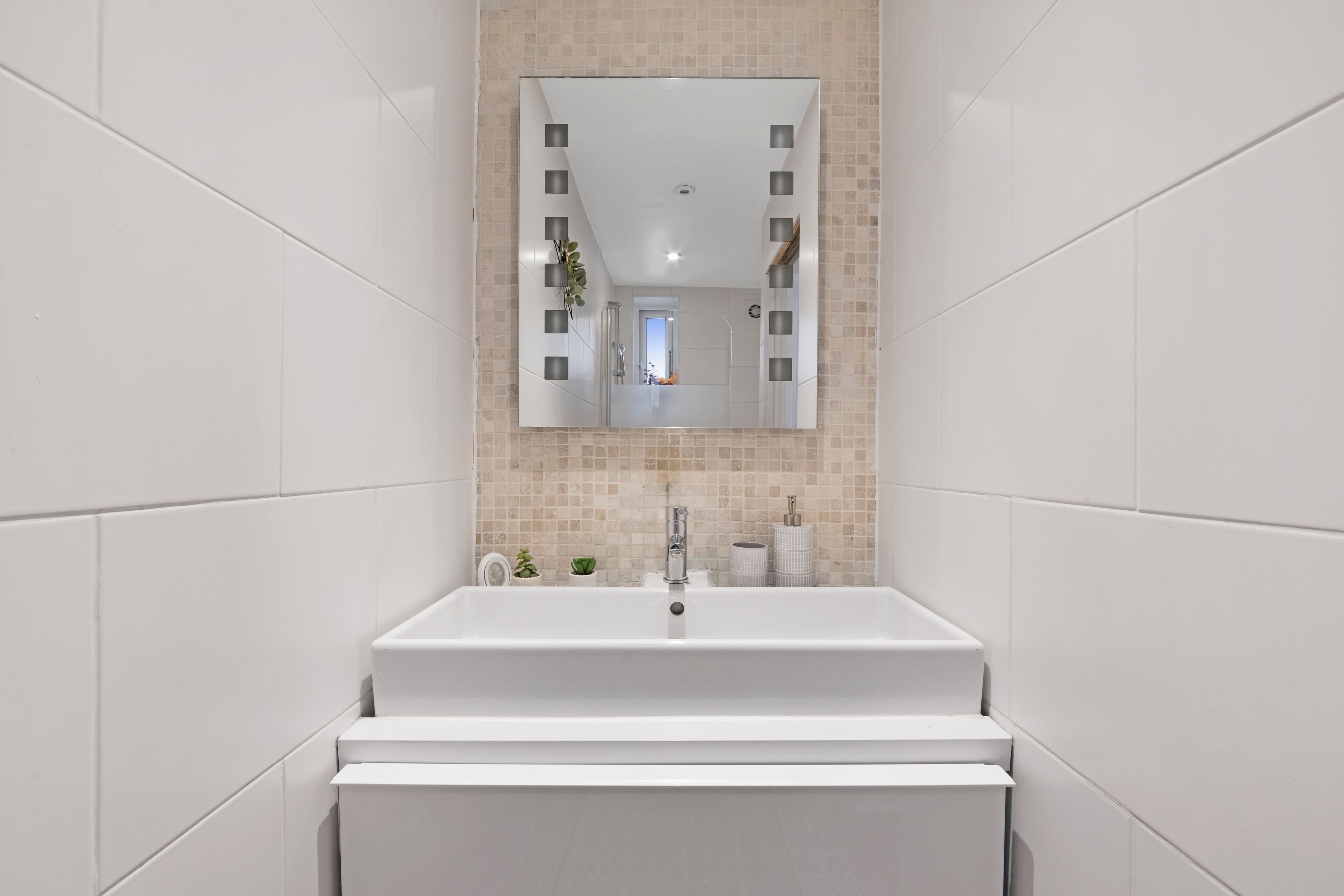 Ein modernes Badezimmer mit einem weißen Waschbecken, einem Spiegel und einer gefliesten Rückwand.