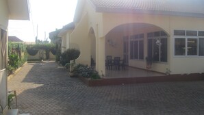 Ein Gebäude mit einem Ziegeldach, einer überdachten Terrasse mit Stühlen und einem gepflasterten Innenhof.