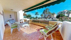 A balcony with a table and chairs, a view of palm trees and buildings, and a tiled floor. - Lovely appartment at 50m from the beach, with swimming pool and beach bar. 4 pers. Wifi. (Dénia)