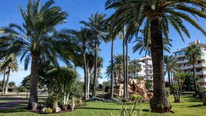 A landscaped garden with palm trees and a building in the background. - Lovely appartment at 50m from the beach, with swimming pool and beach bar. 4 pers. Wifi. (Dénia)