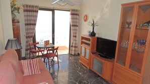 Ein Wohnzimmer mit einer Couch, einem Fernseher und einem Essbereich mit Stühlen und einem Tisch.