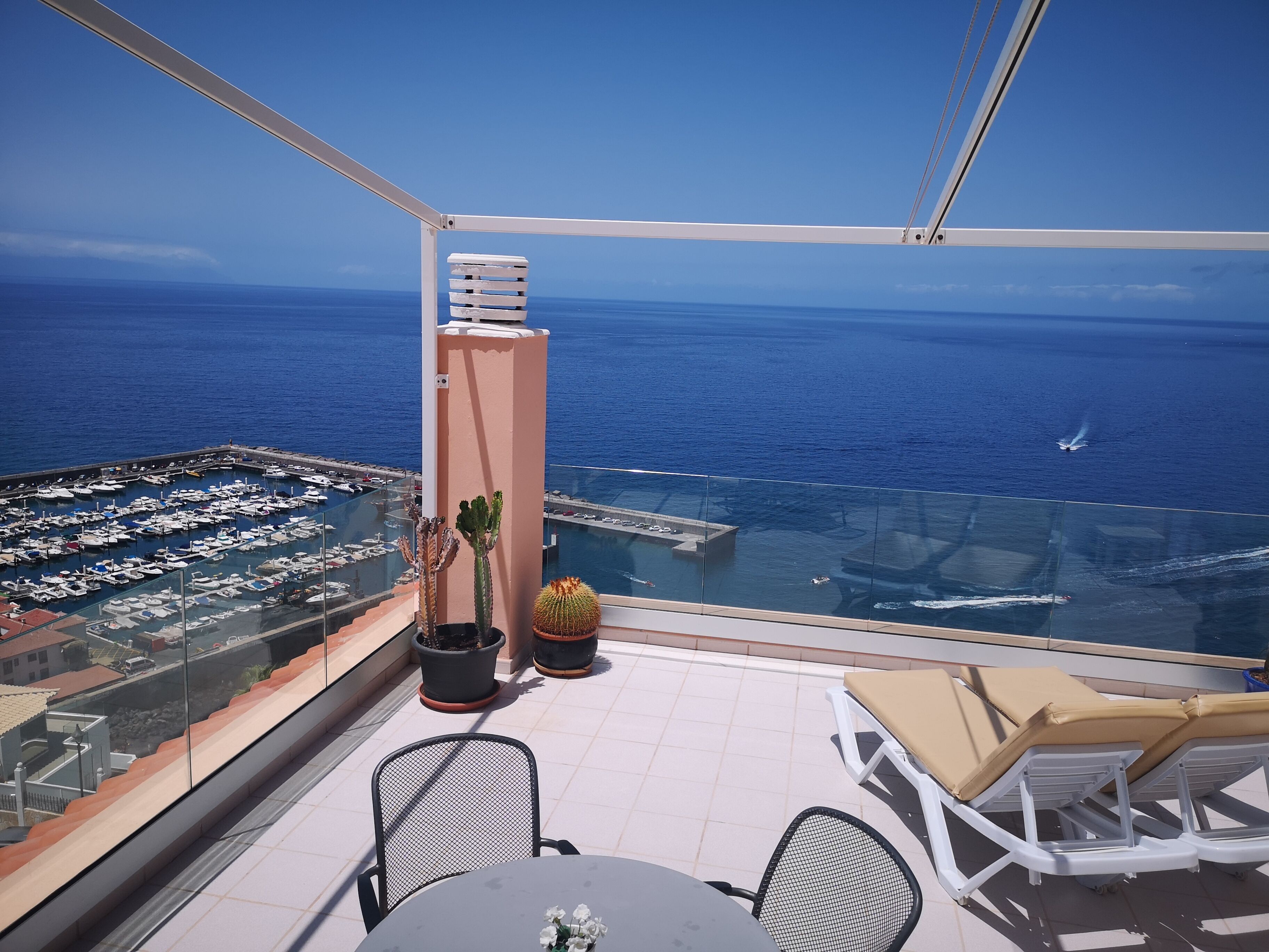A balcony with a view of the sea, a table, chairs, and potted plants.