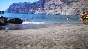 Ein Strand mit klarem, blauem Wasser, felsigen Klippen und ein paar Personen, die schwimmen und spazieren gehen.