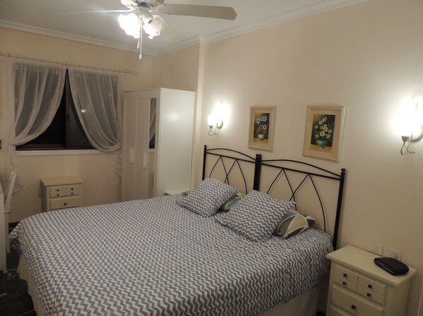 A bedroom with a bed, nightstands, a wardrobe, a ceiling fan, and two wall-mounted light fixtures. - SPECTACULAR SUNNY APARTMENT WITH WIFI, POOL, PANORAMIC CLIFF & SEA VIEWS. (ACANTILADOS LOS GIGANTES)