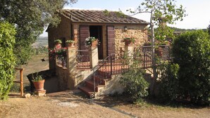 A rustic stone building with a tiled roof, a wooden door, and a small staircase leading to a balcony. There are potted plants and a metal railing around the balcony. - Villa Mulinello, secluded, panoramic view over Montepulciano valley. (torrita di siena, fraz. montefollonico)