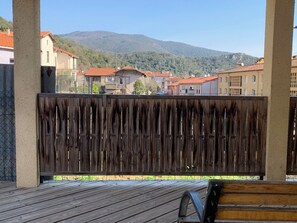 A wooden deck with a bench, a metal railing, and a view of residential buildings and a mountain in the background.