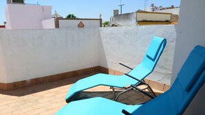 Deux fauteuils bleus sont placés sur une terrasse carrelée, adossée à un mur blanc et bordée d’une murette en briques.