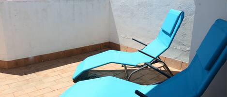Deux fauteuils bleus sont placés sur une terrasse carrelée, adossée à un mur blanc et bordée d’une murette en briques.