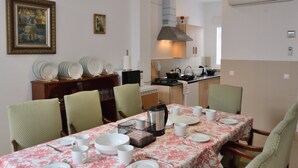 Un coin repas avec une table dressée pour quatre personnes, des chaises, une cafetière et une cuisine en arrière-plan.