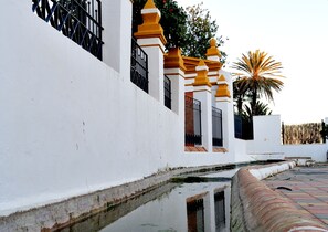 A white building with yellow accents, a gated entrance, and a palm tree in the background.