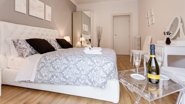 A bedroom with a large bed, a bedside table with a bottle of wine, and a mirror. - Lovely flat next to St. Peter's C. (Roma)
