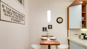 A small kitchen with a dining table set for two, a clock on the wall, and a sign with a humorous message. - Lovely flat next to St. Peter's C. (Roma)