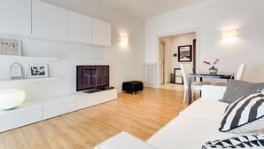 A modern living room with a flat-screen TV, white sofas, a coffee table, and a dining area with a table and chairs. - Lovely flat next to St. Peter's C. (Roma)