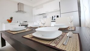 A modern kitchen with white cabinets, a dark wooden table, and a fruit bowl on the counter. - Blue Wave Samui Bophut (Koh Samui)