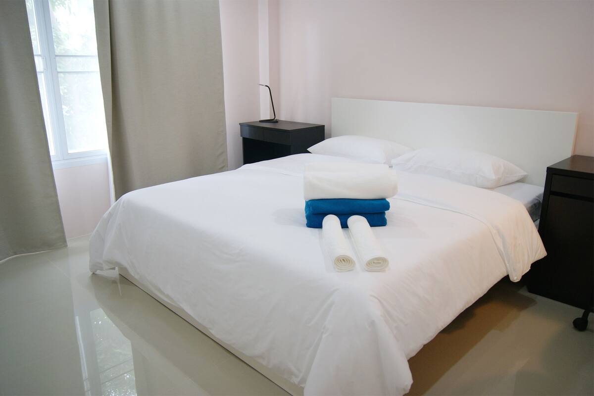 A neatly made bed with white and blue towels, a bedside table, and a nightstand.
