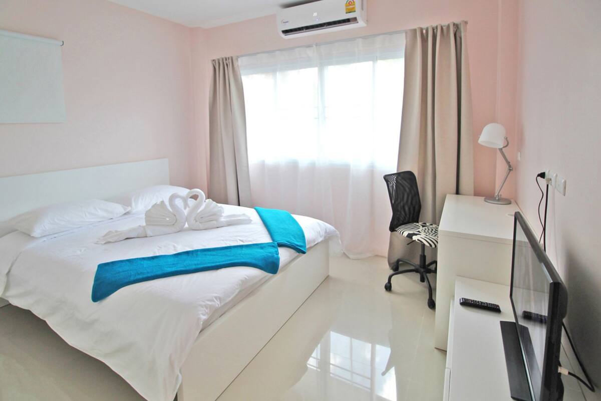 A hotel room with a bed, a desk with a lamp, a chair, and a television.