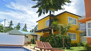 A yellow building with a swimming pool, lounge chairs, and palm trees. - Blue Wave Samui Bophut (Koh Samui)