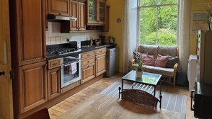 A kitchen with wooden cabinets, a stove, and a window with a view of greenery. - Charming Morningside Flat in Edinburgh (Edinburgh)