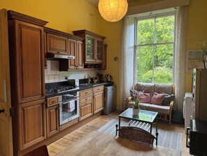 A kitchen with wooden cabinets, a stove, and a window with a view of greenery. - Charming Morningside Flat in Edinburgh (Edinburgh)
