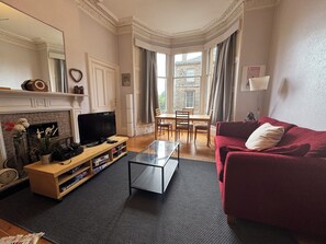 A living room with a television, sofa, and a fireplace. - Charming Morningside Flat in Edinburgh (Edinburgh)