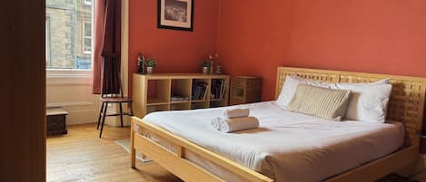 Un dormitorio con cama de madera, un escritorio pequeño, una silla y un ventanal con cortinas.