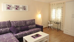 Una sala de estar con un sofá morado, una mesa de centro blanca, una mesa de vidrio con una silla y un armario.