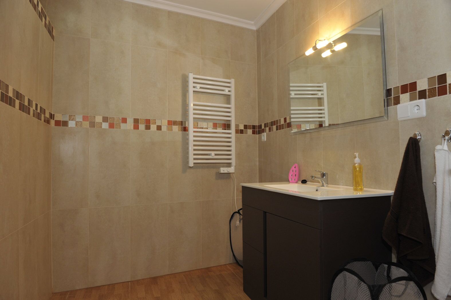 Un baño con piso de baldosas, un lavamanos con espejo, un perchero para toallas y una zona de ducha.