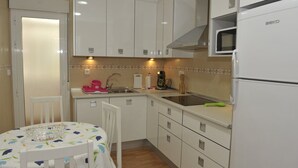 Cocina compacta con armarios blancos, microondas, lavabo y una mesa con mantel floral.