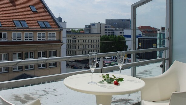 Un balcón con una mesa redonda y dos sillas, con vistas a un paisaje urbano con edificios y cielo despejado.