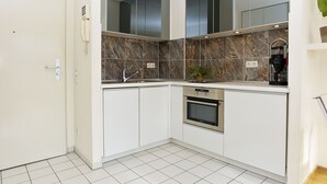Cocina moderna con armarios blancos, horno empotrado, cafetera y salpicadero de mármol.