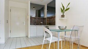 Una cocina moderna con armarios blancos, un salpicadero de mármol y un comedor con mesa de vidrio y sillas transparentes.