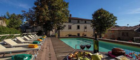 A poolside area with lounge chairs, a table with fruits and drinks, and a view of buildings in the background.
