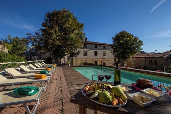 A poolside area with lounge chairs, a table with fruits and drinks, and a view of buildings in the background.