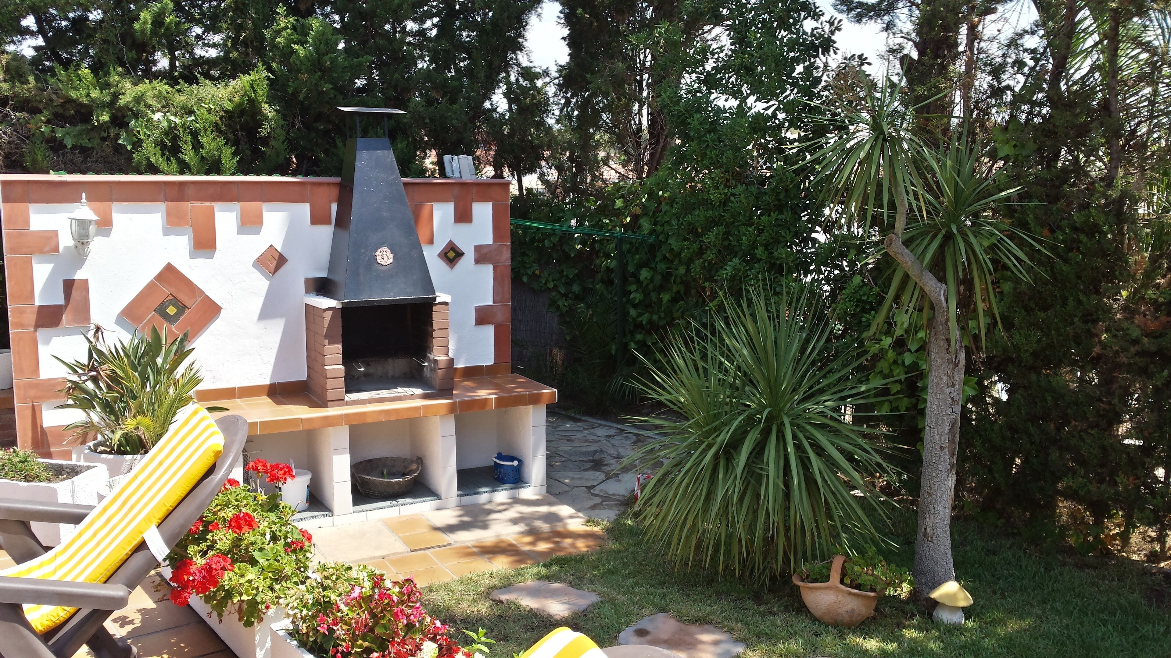 A brick-built outdoor kitchen with a chimney, surrounded by potted plants and a stone pathway.