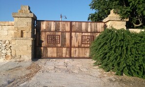Un portón de madera rústico con rejas de metal, un muro de piedra y un arbusto grande.