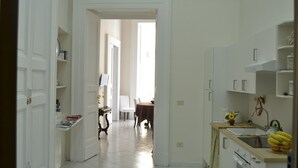 A kitchen with white cabinets, a dining area with a table and chairs, and a view into another room. - Comfortable apartment in the historic center of Naples close to everything (Napoli)