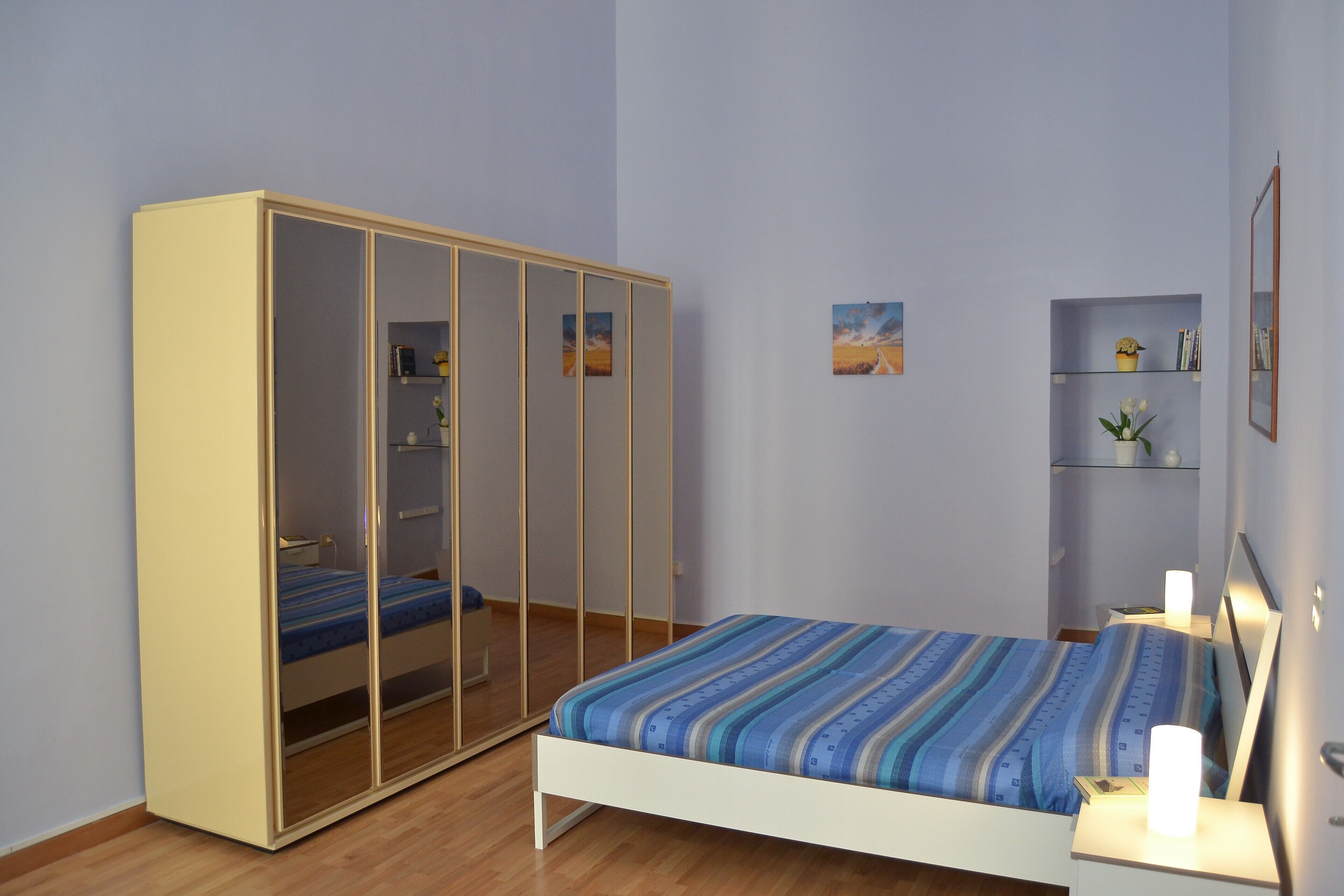 Un dormitorio con cama, armario, mesita de noche y estante decorado con objetos.