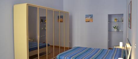 Un dormitorio con cama, armario, mesita de noche y estante decorado con objetos.