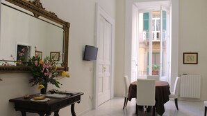 A dining area with a table and chairs, a mirror, a television, and a vase with flowers. - Comfortable apartment in the historic center of Naples close to everything (Napoli)