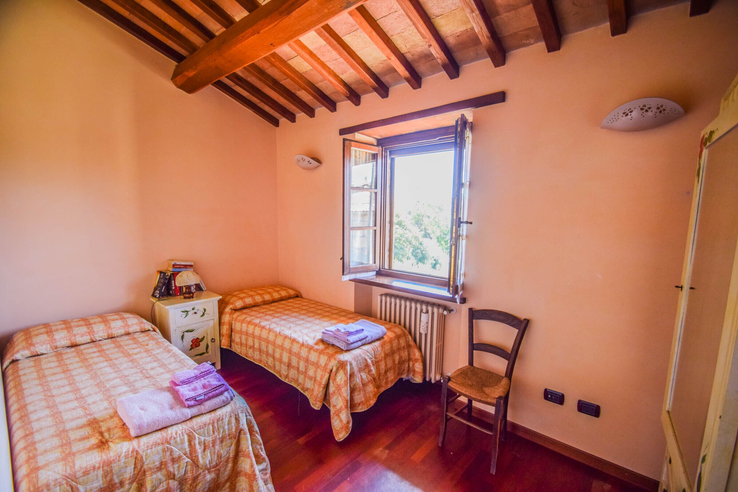 Una habitación con dos camas, una silla, un ventanal y un radiador.