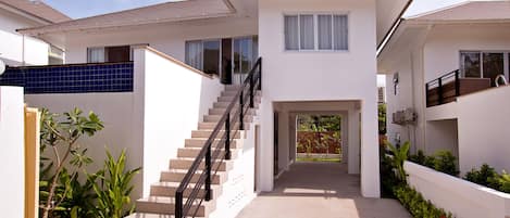 A modern two-story house with a central staircase, a covered outdoor area, and a garden with various plants.