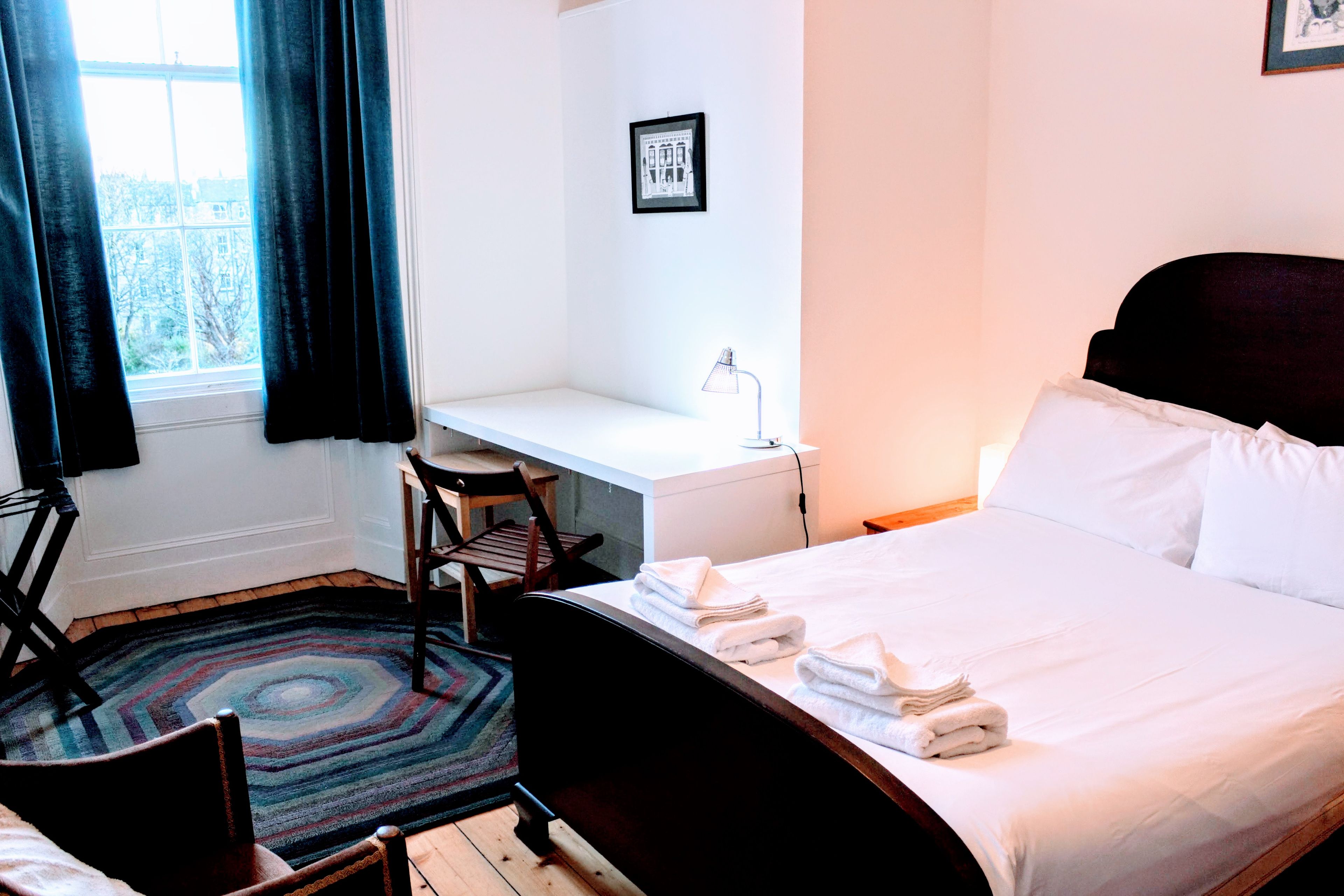 A hotel room with a bed, a desk, a chair, and a window with curtains.