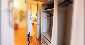A hallway with a wooden floor, a closet with hanging clothes, and a door leading to another room. - Classic 5BDR Flat Overlooking Bruntsfield Links (Edinburgh)