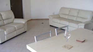A dining area with a wooden table, two white sofas, and a glass of wine.